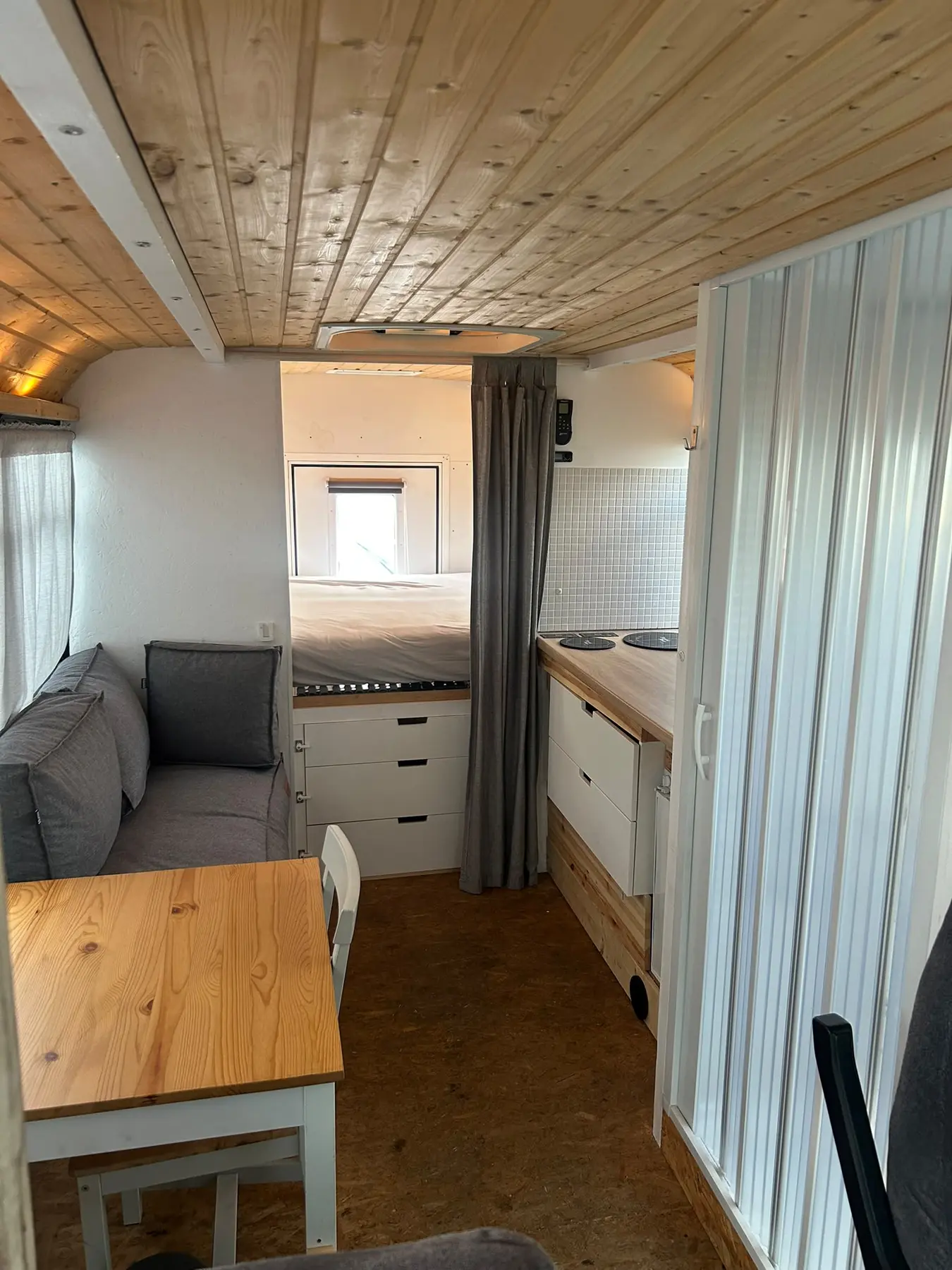 Wohnbereich mit Sitzbank, Tisch, Küche und Doppelbett